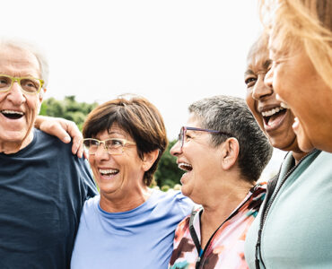 A group of adults ages 65 and up, standing together in a semi-circle and laughing.