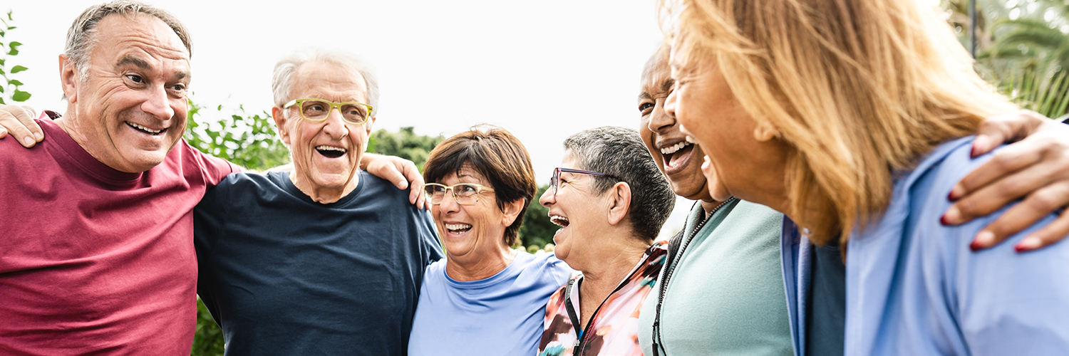 A group of adults ages 65 and up, standing together in a semi-circle and laughing.