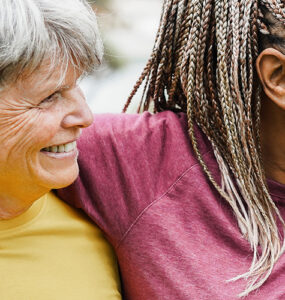 Four women over 50 of various ethnicities hugging together and smiling.
