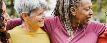 Four women over 50 of various ethnicities hugging together and smiling.