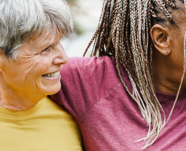 Four women over 50 of various ethnicities hugging together and smiling.