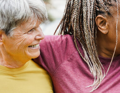 Four women over 50 of various ethnicities hugging together and smiling.