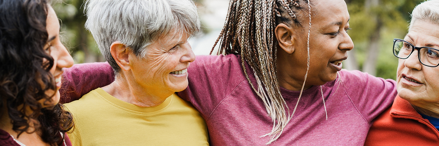 Four women over 50 of various ethnicities hugging together and smiling.