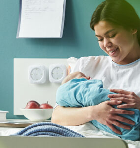young woman sitting in hospital bed holding and breastfeeding newborn baby