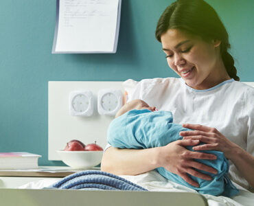 young woman sitting in hospital bed holding and breastfeeding newborn baby