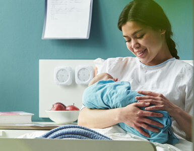young woman sitting in hospital bed holding and breastfeeding newborn baby