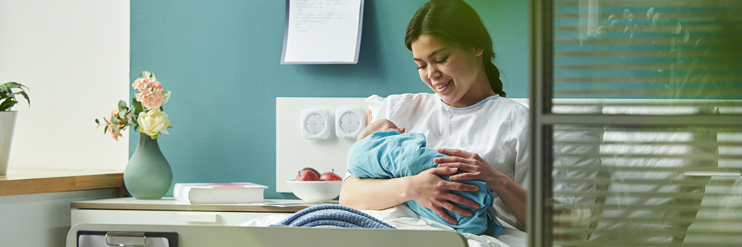 young woman sitting in hospital bed holding and breastfeeding newborn baby