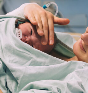 A woman holding her newborn baby, who is laying on her chest, in a hospital bed.