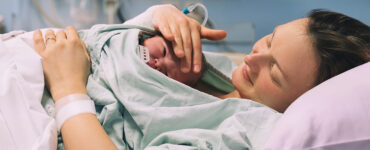 A woman holding her newborn baby, who is laying on her chest, in a hospital bed.