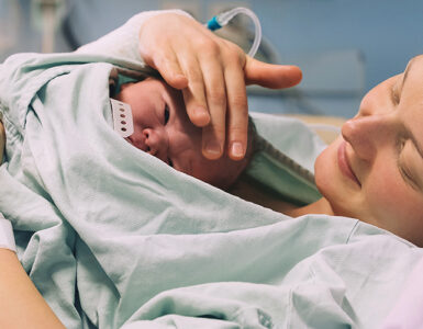 A woman holding her newborn baby, who is laying on her chest, in a hospital bed.