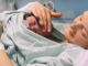 A woman holding her newborn baby, who is laying on her chest, in a hospital bed.