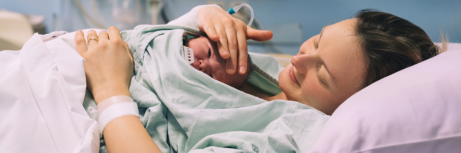 A woman holding her newborn baby, who is laying on her chest, in a hospital bed.