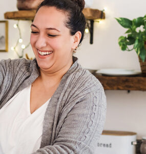 A young woman standing in her kitchen, making a healthy green smoothie.