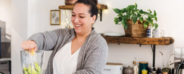 A young woman standing in her kitchen, making a healthy green smoothie.