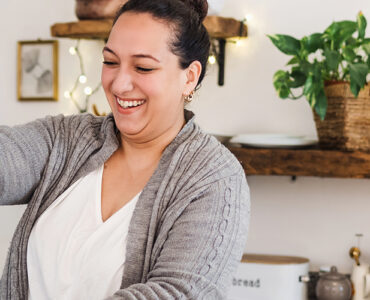 A young woman standing in her kitchen, making a healthy green smoothie.