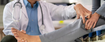 A doctor is helping a patient with a foot injury. The patient is wearing a gray and white outfit.