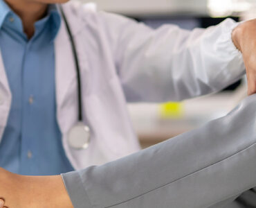 A doctor is helping a patient with a foot injury. The patient is wearing a gray and white outfit.