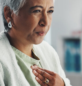 Senior, sick woman heartburn with symptoms for discomfort, acid reflux or viral gastro disease at hospital.