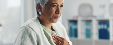 Senior, sick woman heartburn with symptoms for discomfort, acid reflux or viral gastro disease at hospital.
