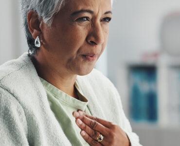 Senior, sick woman heartburn with symptoms for discomfort, acid reflux or viral gastro disease at hospital.