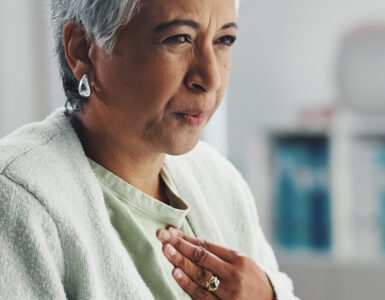 Senior, sick woman heartburn with symptoms for discomfort, acid reflux or viral gastro disease at hospital.