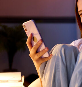 Teenage girl sitting at a desk in her bedroom at night looking at a mobile phone, illustrating teen screen time.