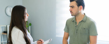 A young man speaking to a female physician inside a medical office.