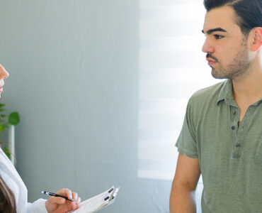 A young man speaking to a female physician inside a medical office.