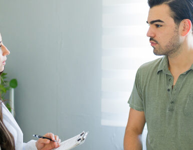 A young man speaking to a female physician inside a medical office.
