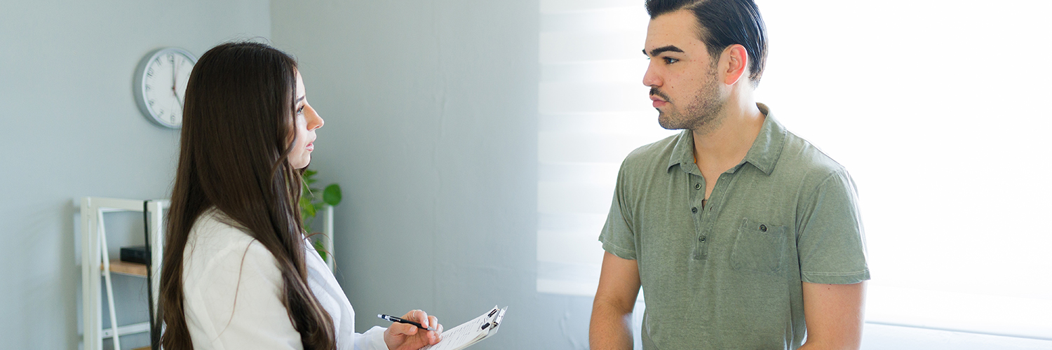 A young man speaking to a female physician inside a medical office.