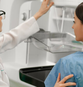 A female patient standing next to a female doctor while getting a mammogram.