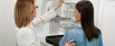 A female patient standing next to a female doctor while getting a mammogram.