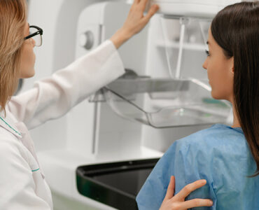 A female patient standing next to a female doctor while getting a mammogram.
