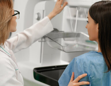 A female patient standing next to a female doctor while getting a mammogram.