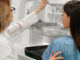 A female patient standing next to a female doctor while getting a mammogram.