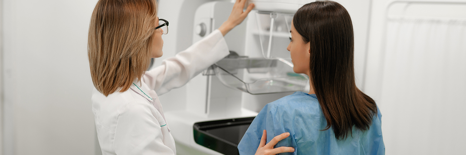 A female patient standing next to a female doctor while getting a mammogram.