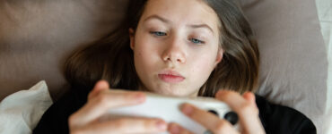 Teenage girl lying in bed using a smartphone.