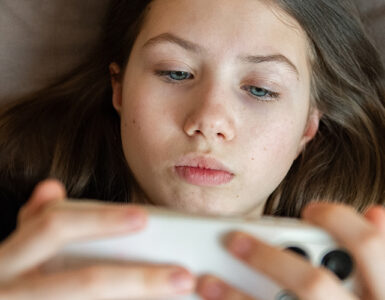 Teenage girl lying in bed using a smartphone.