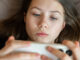 Teenage girl lying in bed using a smartphone.