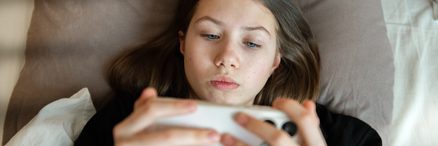 Teenage girl lying in bed using a smartphone.